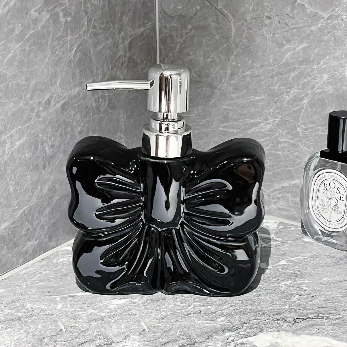 A black ceramic pump dispenser bottle with a bowknot design and silver pump mechanism on a gray stone surface.