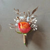 Boutonnière en soie orange vintage avec une rose et un feuillage argenté avec des accents de perles.