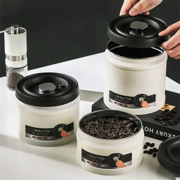 A hand is opening a white storage canister with a black lid, showing dark coffee beans inside.
