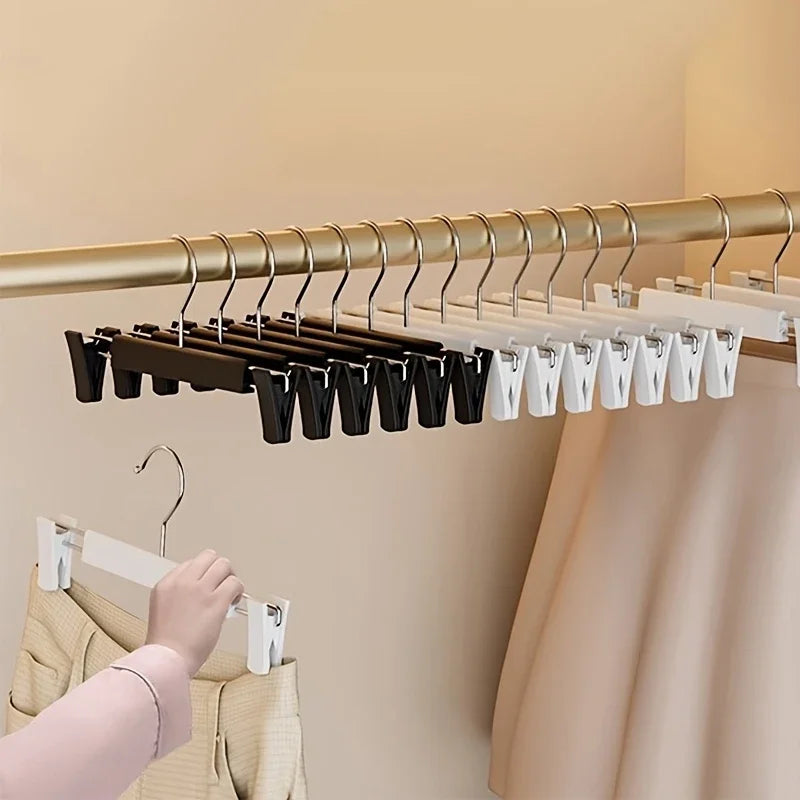 A close-up view of adjustable wooden clothes hangers with various sized hooks and white plastic hangers hanging from a metal 