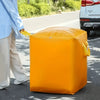 A bright orange heavy-duty waterproof storage bag is being carried by a person on an asphalt road.