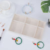 A light beige velvet jewelry organizer tray with multiple compartments and several delicate beaded bracelets is displayed on 