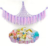 A bohemian stuffed animal hammock featuring purple and pink fringe decorations.