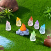 A collection of luminous resin mini fairy gnomes in various colors like yellow, orange, purple, and blue resting on green mos