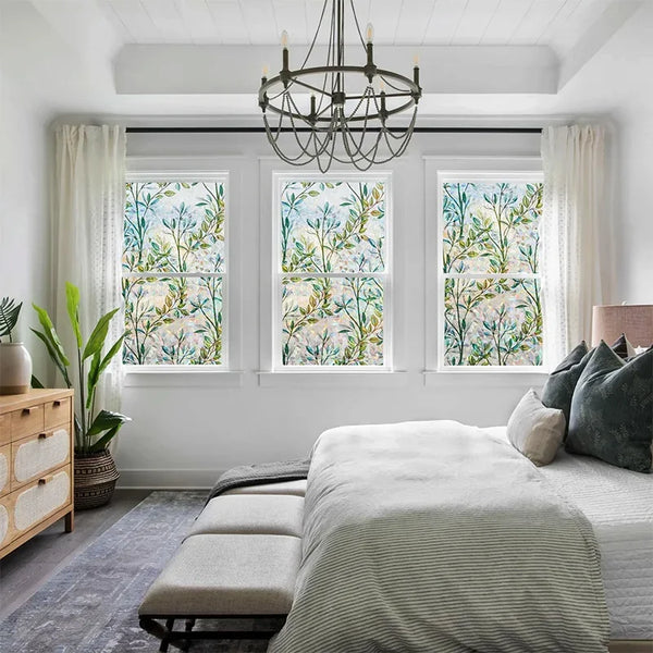 A bedroom featuring a bed with striped linens and sheer curtains, overlooking windows decorated with green vines.