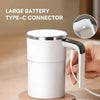 A white electric self-stirring coffee mug with a large Type-C connector is shown being held by a hand.