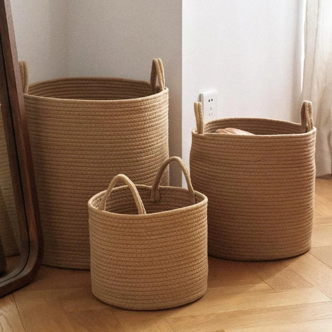 Three natural woven cotton rope storage baskets of varying sizes on a wooden floor.