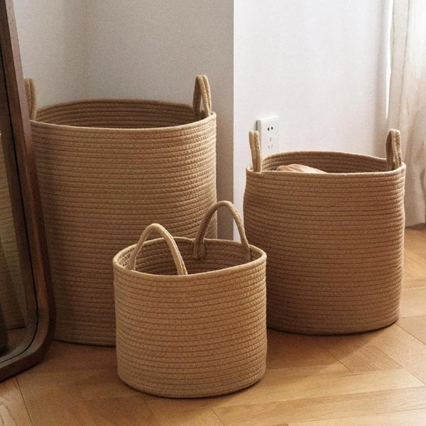 Three natural woven cotton rope storage baskets of varying sizes on a wooden floor.