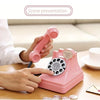 A hand is operating a pink retro phone money jar photography prop on a wooden table.