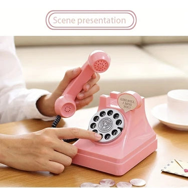 A hand is operating a pink retro phone money jar photography prop on a wooden table.