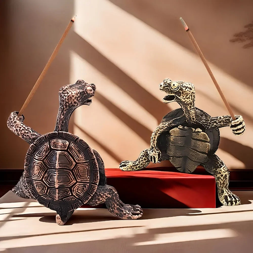 Une petite figurine de tortue en métal repose sur une surface rouge avec des ombres projetées par la lumière du soleil.