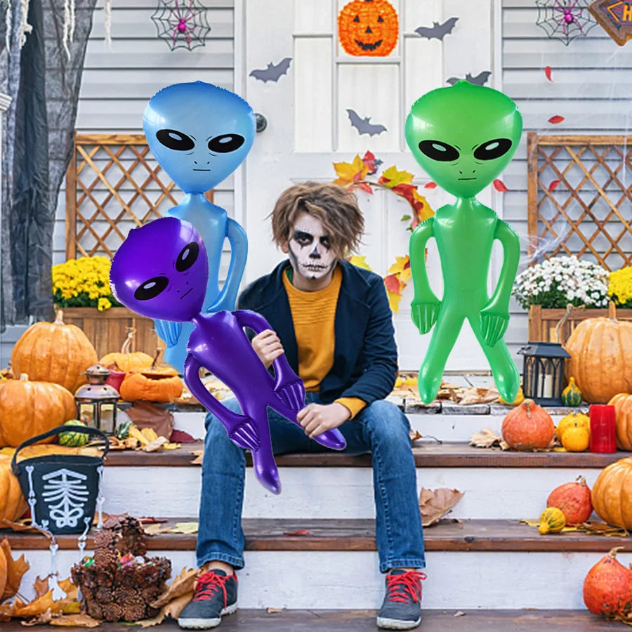A person dressed as an alien sits on wooden steps in front of a white door decorated with Halloween elements.