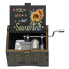 A small wooden music box with a dark lid featuring text and a sunflower design, housed in a wooden box.