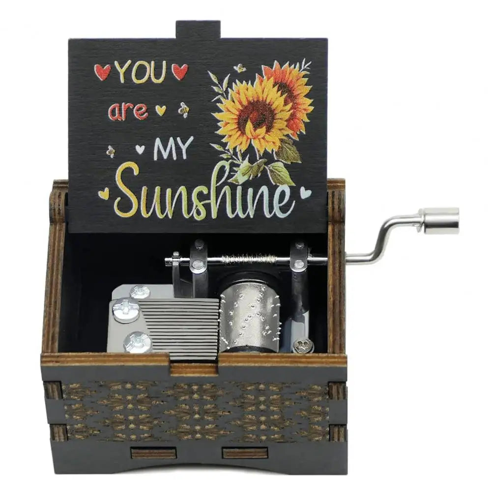 A small wooden music box with a dark lid featuring text and a sunflower design, housed in a wooden box.