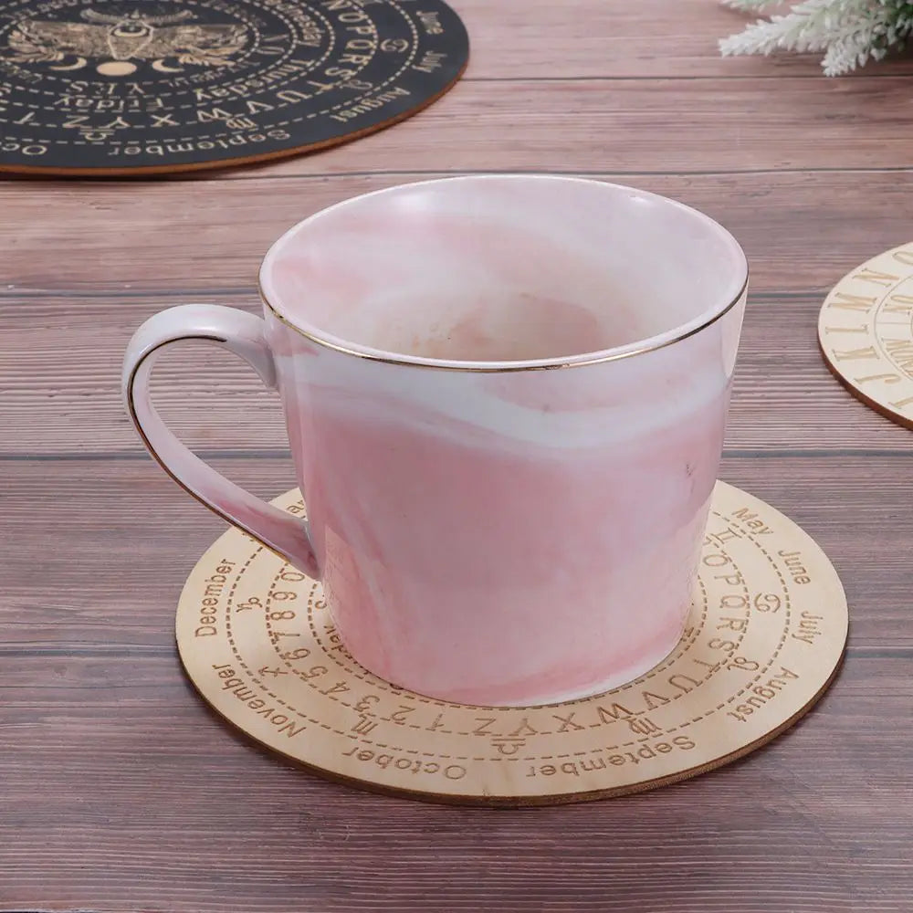 Pinke Keramiktasse mit goldener Umrandung auf einem Holzpendelbrett mit Monaten