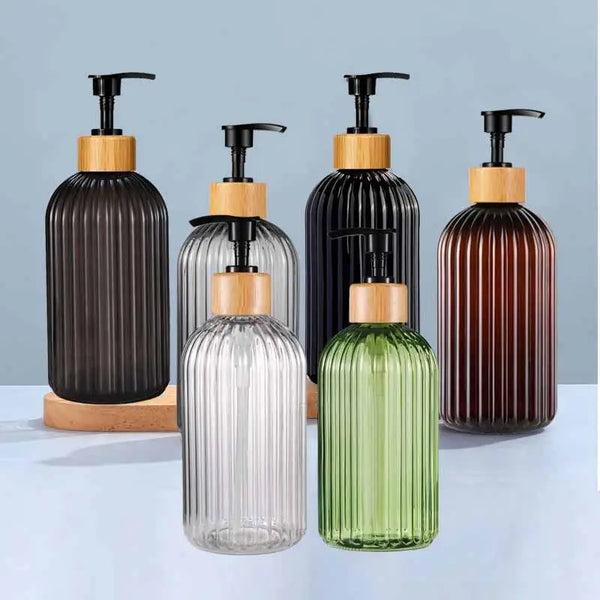 A set of four refillable glass soap dispensers with black and green glass bodies and wooden pump tops.