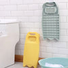 A light green plastic washing board with a soap holder is mounted on a white tiled wall next to a toilet.