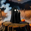 A black ghost statue decoration with glowing eyes sits on a wooden log in a dark, spooky outdoor setting.