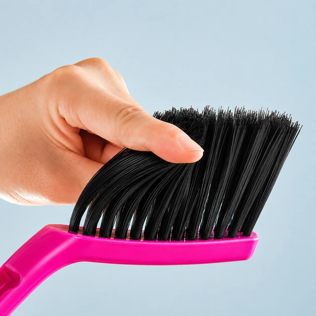 A hand holds a pink mini handheld dustpan and brush set with black bristles against a light blue background.