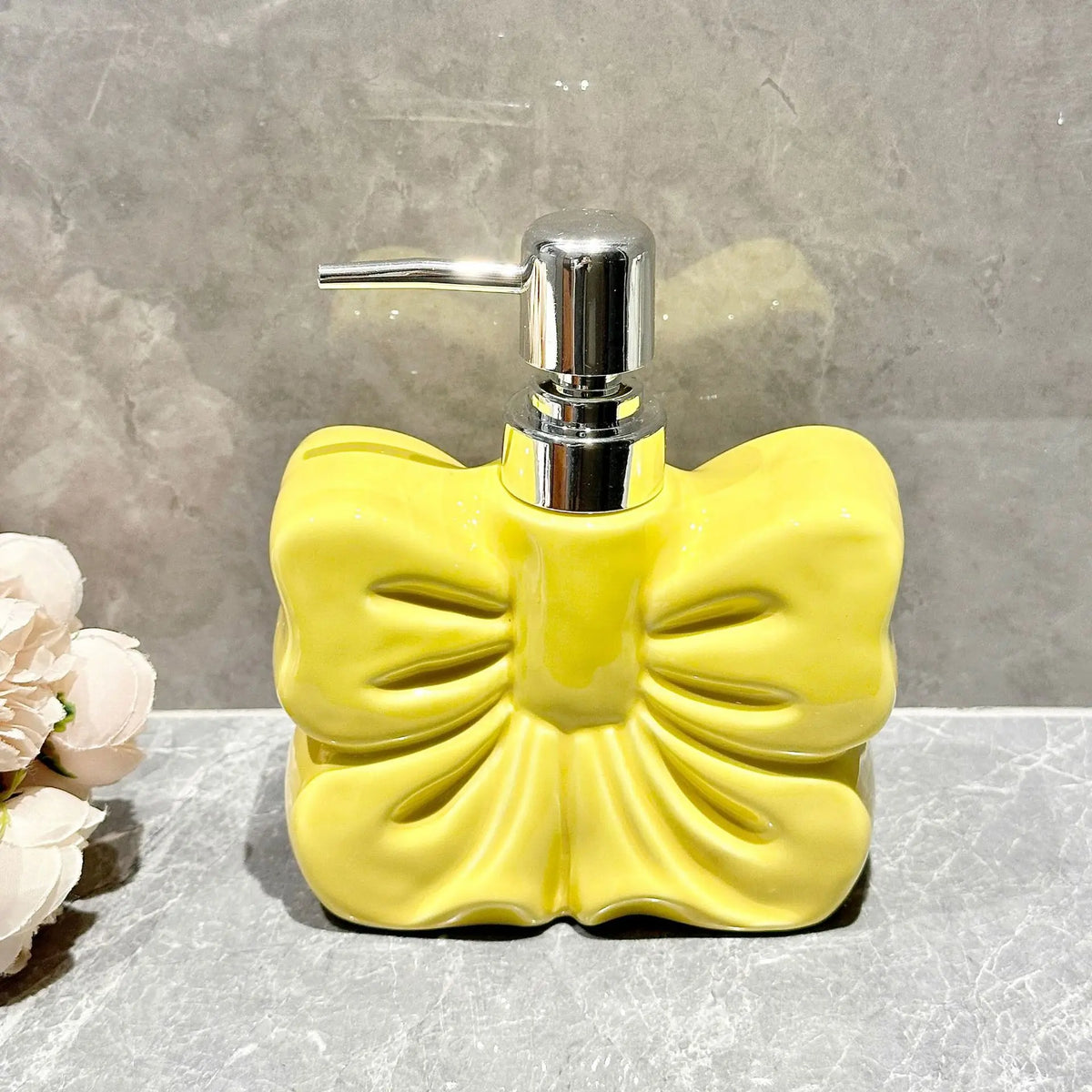 A yellow ceramic pump dispenser bottle with a bowknot design and silver pump top.
