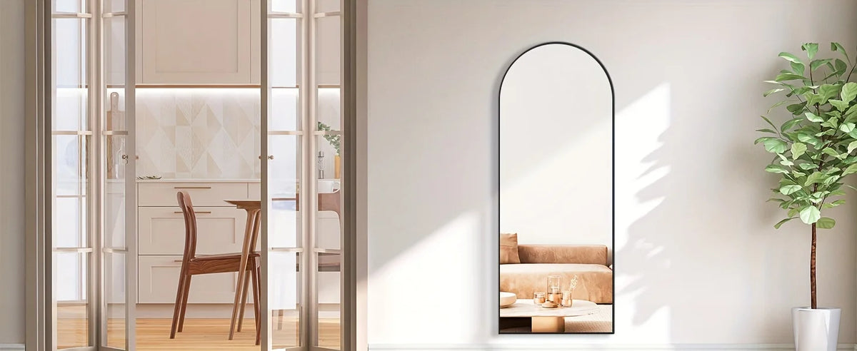 A full length arch mirror with an aluminum frame reflecting a room interior and a potted plant.