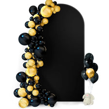 A black arch backdrop decorated with gold and black balloons and a small stuffed animal.