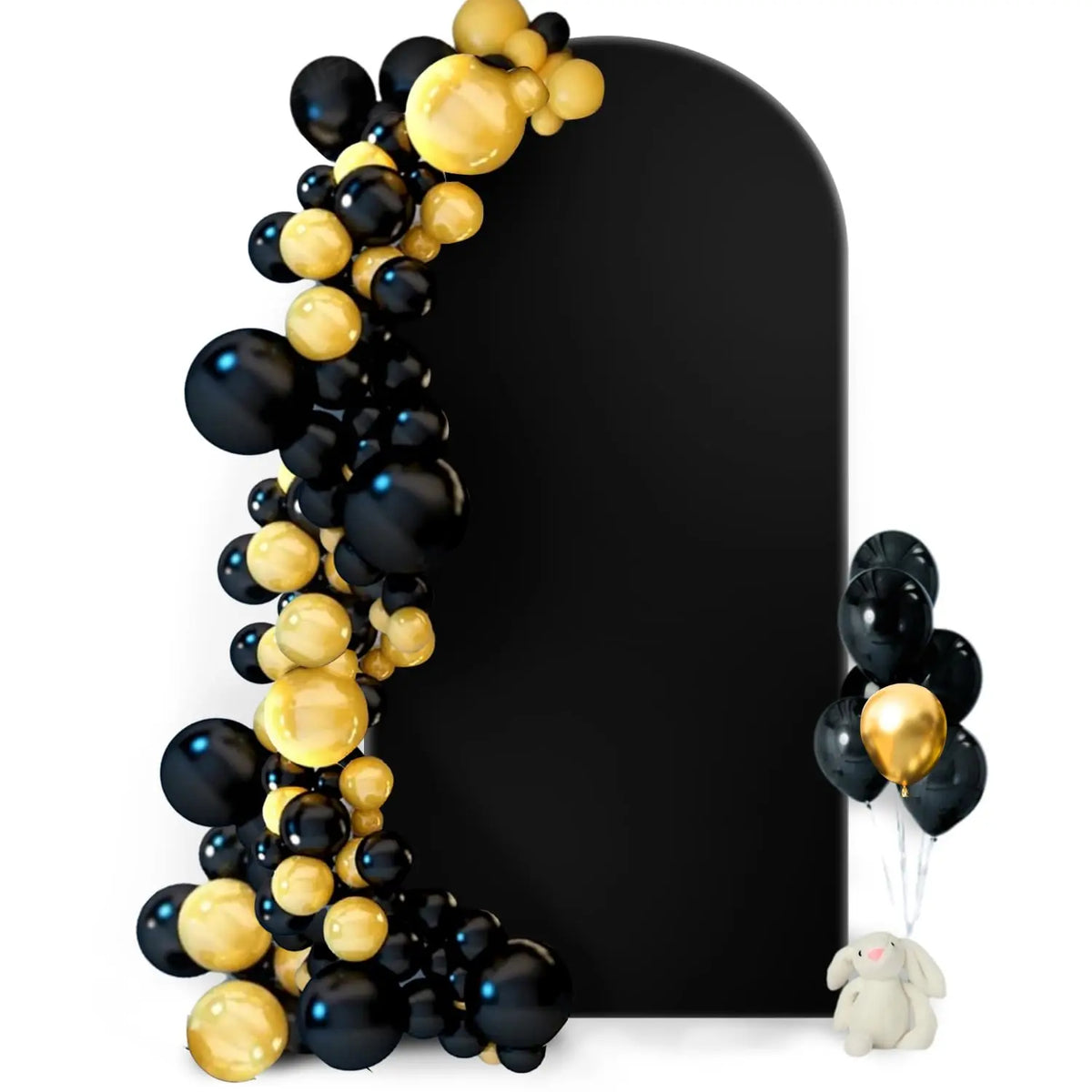 A black arch backdrop decorated with gold and black balloons and a small stuffed animal.