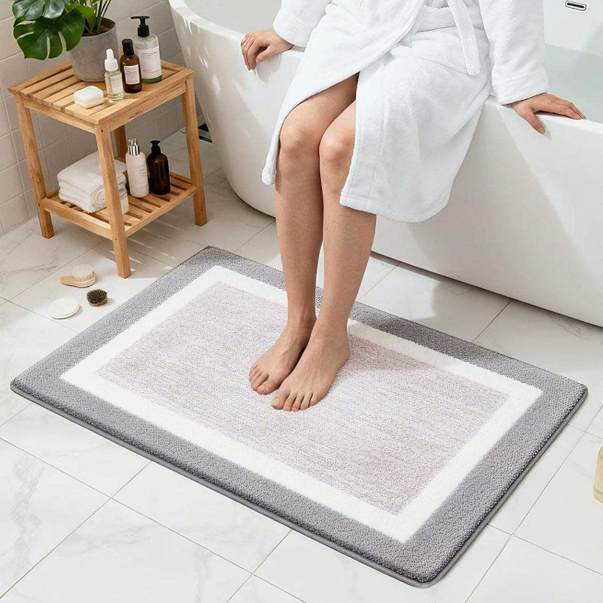 A white bathrobe is shown sitting on a bathtub edge, with a gray microfiber bath mat placed on the floor.