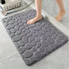 A gray, textured 3D non-slip bathroom doormat is placed on a light-colored tile floor.