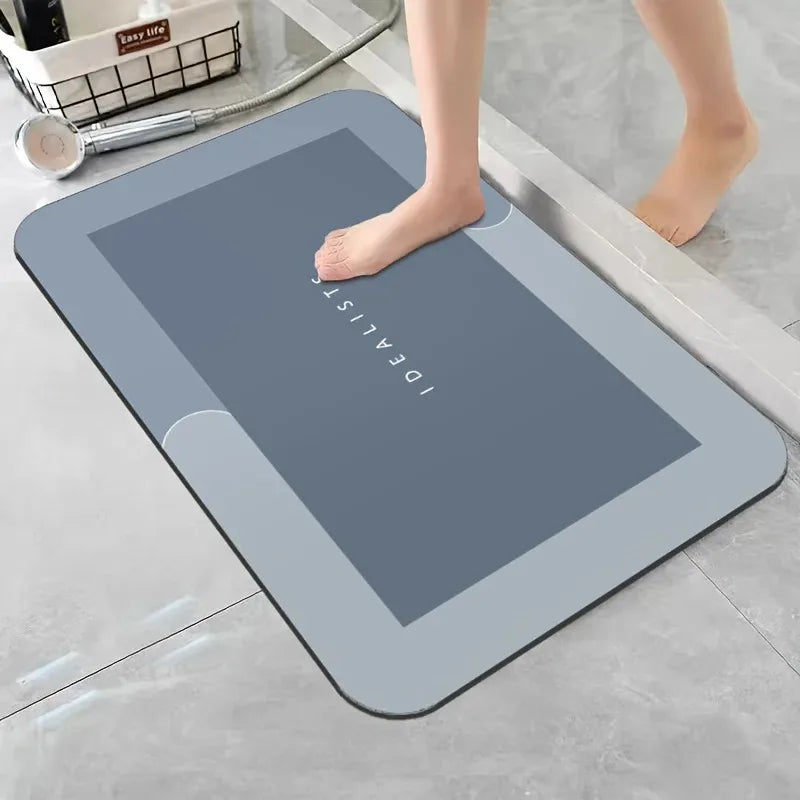 A gray diatomaceous earth absorbent bath mat is placed on a light gray floor next to a person's bare foot.