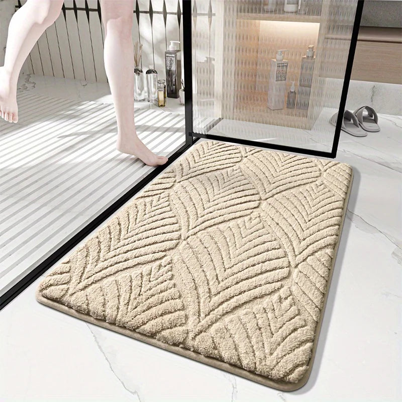A beige plush non-slip bathroom rug is shown on a white marble floor next to a glass panel.