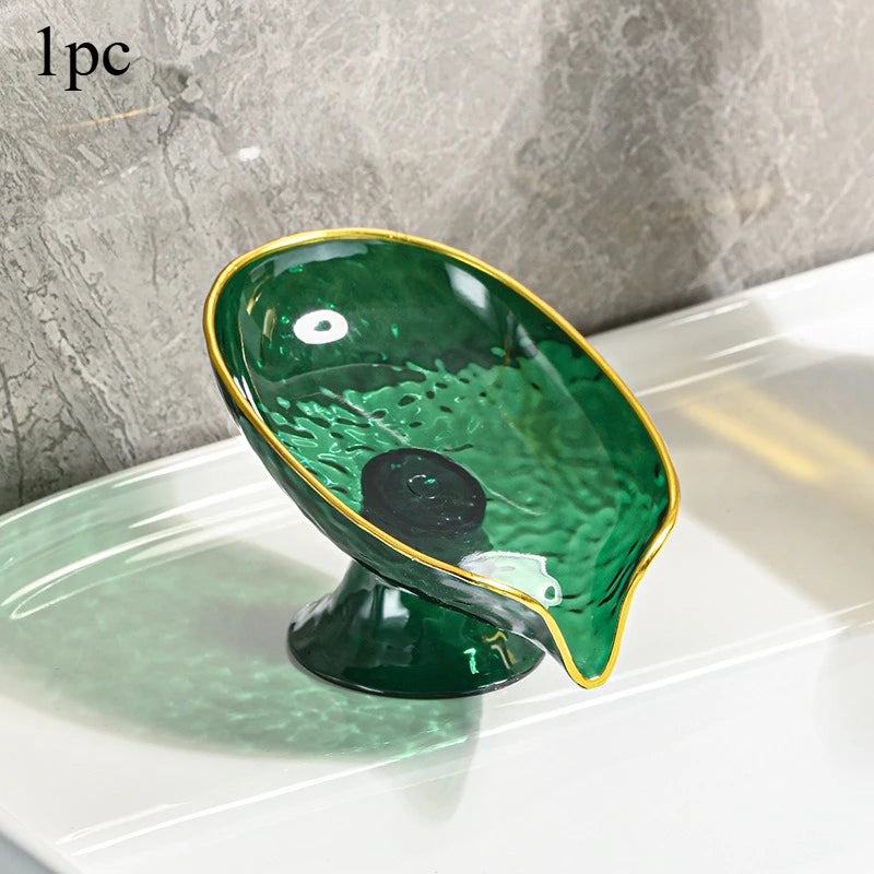 A glossy green oval plastic soap dish with a gold rim and drainage holes resting on a white tray.