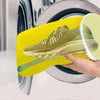A hand holds a yellow reusable shoe washing bag with soft bristles over a plate.