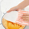 A hand is dipping a microfiber kitchen dish cloth into a bowl of orange-colored liquid for cleaning.