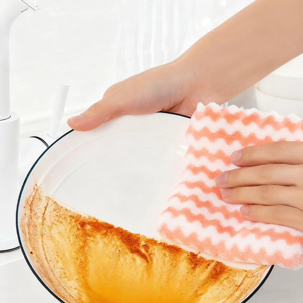 A hand is dipping a microfiber kitchen dish cloth into a bowl of orange-colored liquid for cleaning.