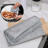 A stack of gray thickened steel wire cleaning cloths is shown next to a plate with food residue.