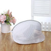 A white mesh laundry bag for shoes and delicates with a zipper resting on a wooden surface.
