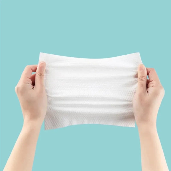 Hands holding a white disposable cotton face wipe against a light blue background.