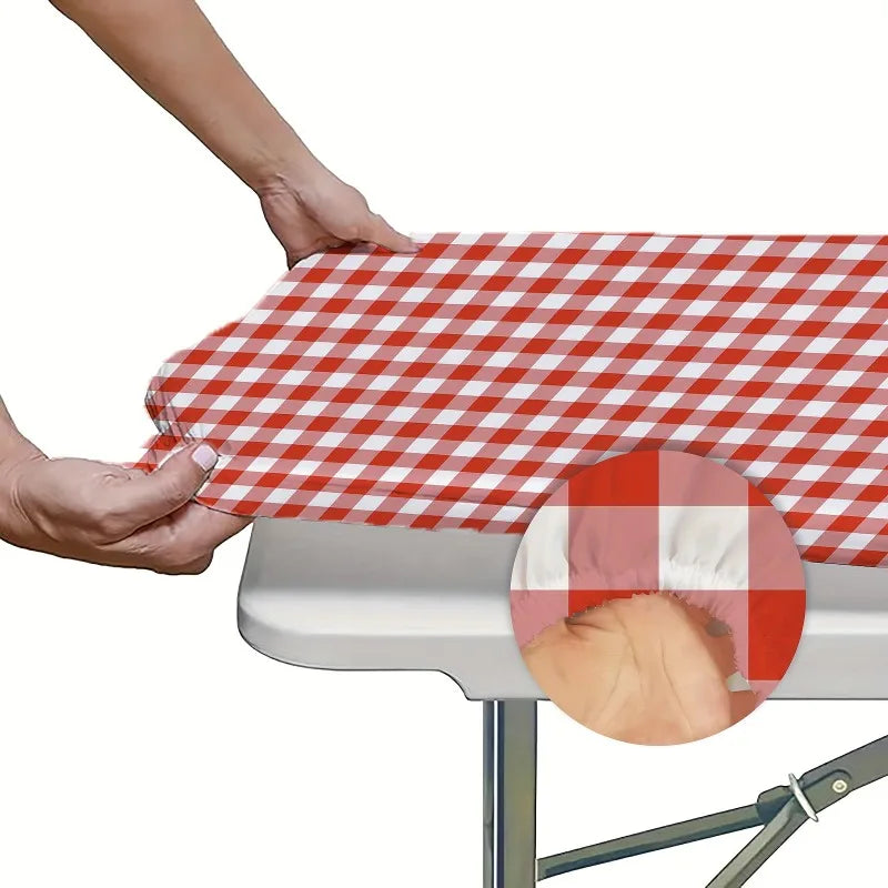 A hand is placing a red and white plaid tablecloth onto a gray table.