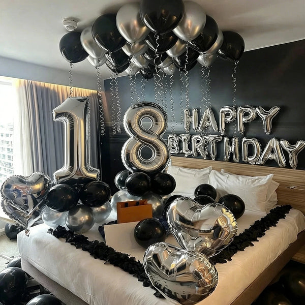 A silver and black balloon garland decor is displayed against a dark wall for a birthday celebration.