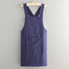 A dark indigo cotton kitchen apron hanging on a wooden hanger against a light gray background.