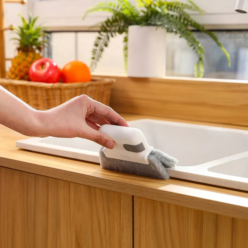 A hand is placing a gray cleaning brush into a white sink basin for cleaning.