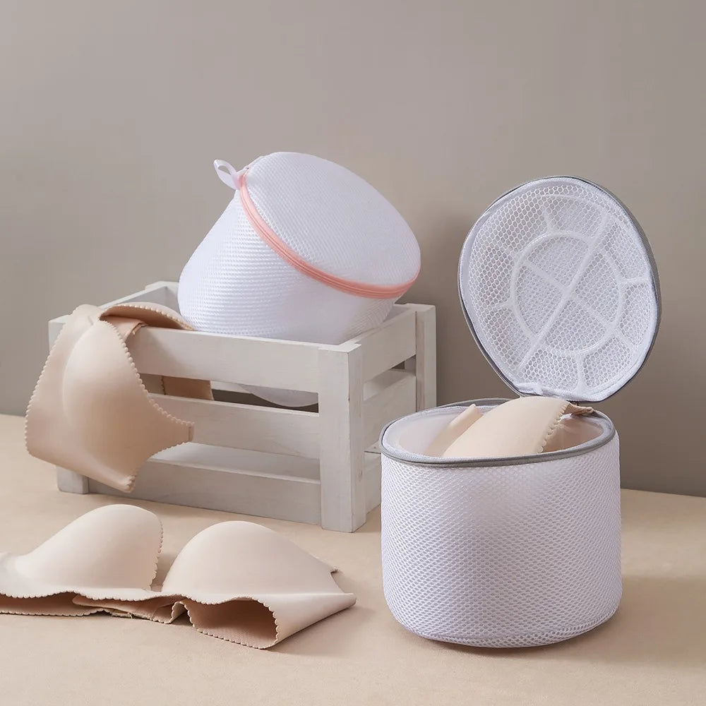 A white reusable zippered laundry bag with a pink trim is shown next to a cylindrical storage container and folded fabric.