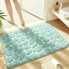 A teal soft pebble embossed bathroom rug placed on a wooden floor next to a shower area.