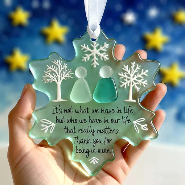 A handcrafted sea glass snowflake ornament with a quote about who matters, held in a hand against a blue snowy background.