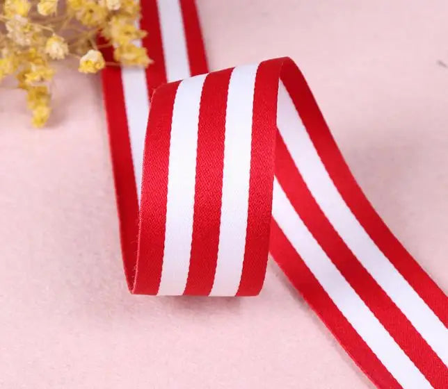 Red and white striped grosgrain ribbon rolled and laid on a light pink surface.