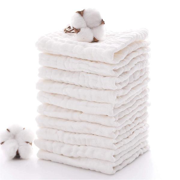 A stack of white natural cotton muslin washcloths with a fluffy cotton ball on top.