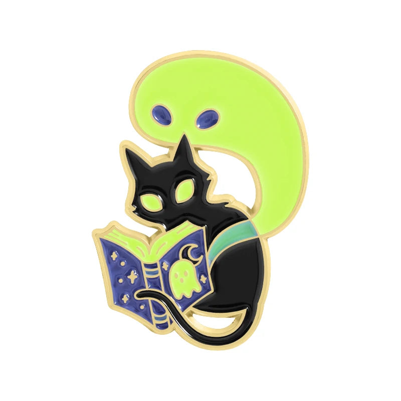Pin de esmalte negro con cabeza de gato y orejas verdes brillantes y un libro amarillo.
