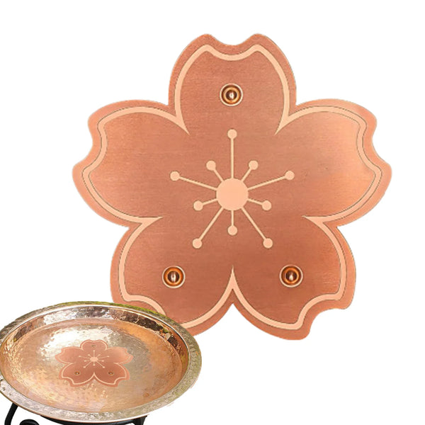 A copper bird bath disk with a floral design and triple-point support is shown next to its base.
