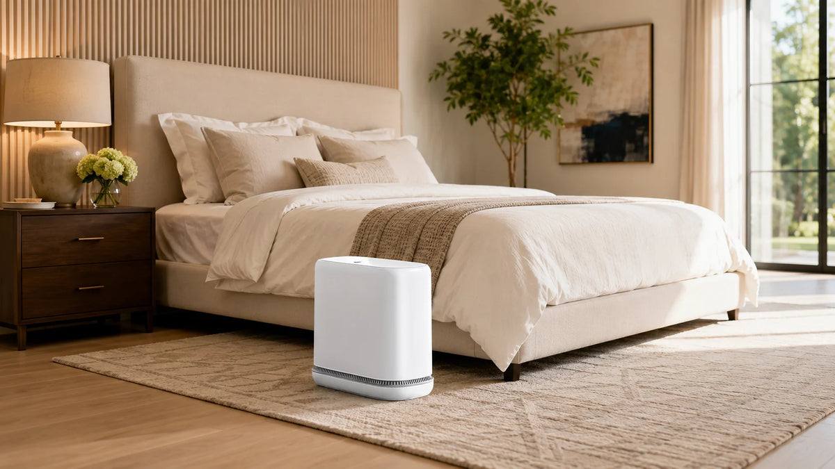 A white slim hands-free trash can with a one-press lid sits on a light wood floor in a modern bedroom setting.